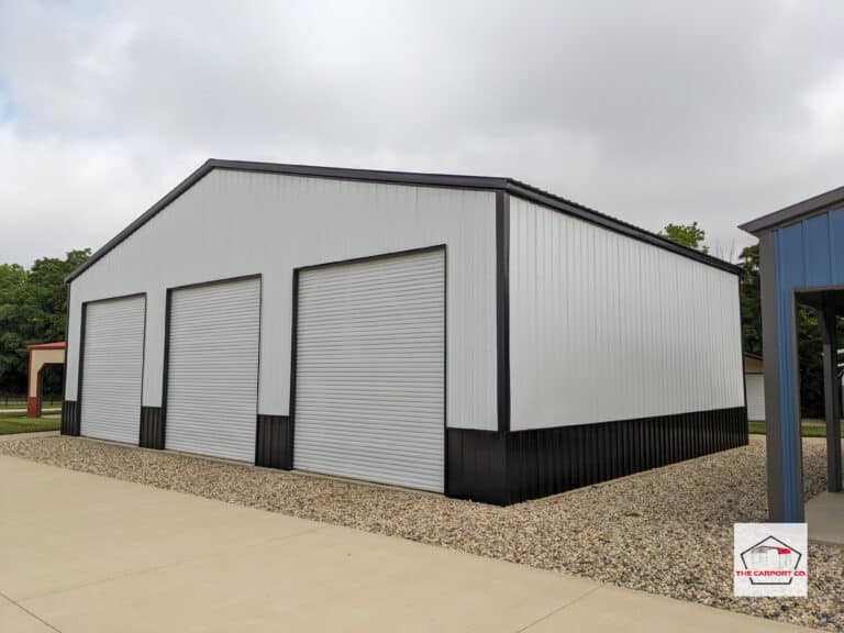 Corner of white with black two tone AKA wainscoting (white on top/black on bottom) commercial truss wide span building with vertical siding and three 12x12 roll up doors.