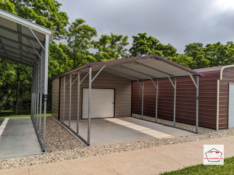 Corner of a wind-resistant engineer stamped and certified metal carport with back metal storage unit. Back storage unit is fully enclosed and has 6x6 roll up door on front end. The carport portion has a horizontal a-frame roof. Structure has burgundy trim and tan siding.