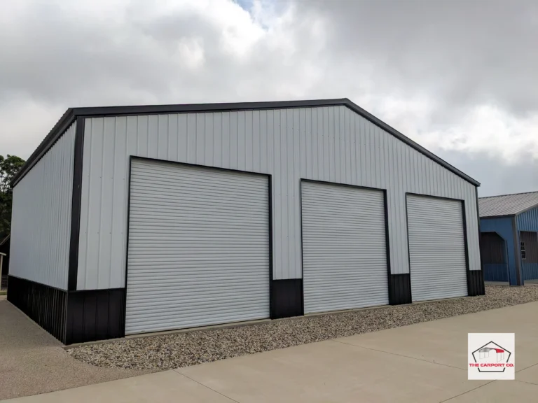 Corner of white with black two tone AKA wainscoting (white on top/black on bottom) commercial truss wide span building by The Carport Co. with vertical siding and three 12x12 roll up doors.