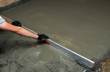 Man dragging a trowel across wet concrete to finish it and ensure it cures level and smooth.