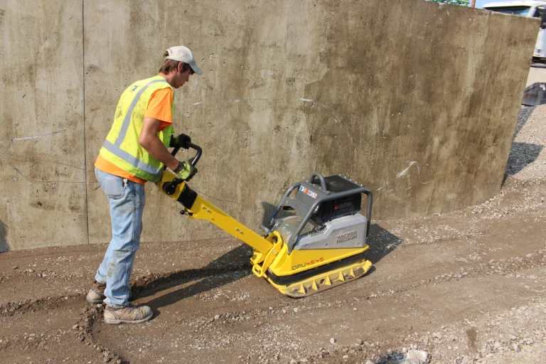 Construction worker compacting gravel with gravel compactor. The gravel will sit underneath a concrete slab.