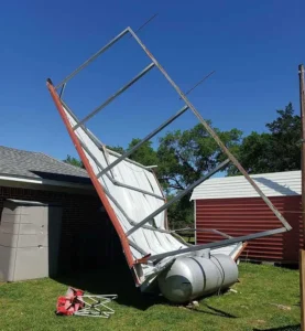 Photo showcasing a metal carport that has been ripped out of the ground from high winds during a hurricane or tornado. The main culprit in this instance was incorrect anchoring.