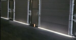 Photo of prefabricated metal garage building with three roll up doors that have gaps underneath the door and around the roll-up door allowing light, moisture, dust, and the elements into the building.