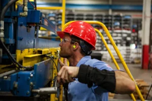 Steel structure and metal building manufacturing workshop with worker cutting galvanized steel tubing. Galvanized steel tubing is used in carports, garages, sheds, lean-tos, commercial buidlings, etc.